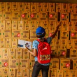 Seorang wanita memegang clipboard sedang menghitung stok barang di gudang penuh kotak